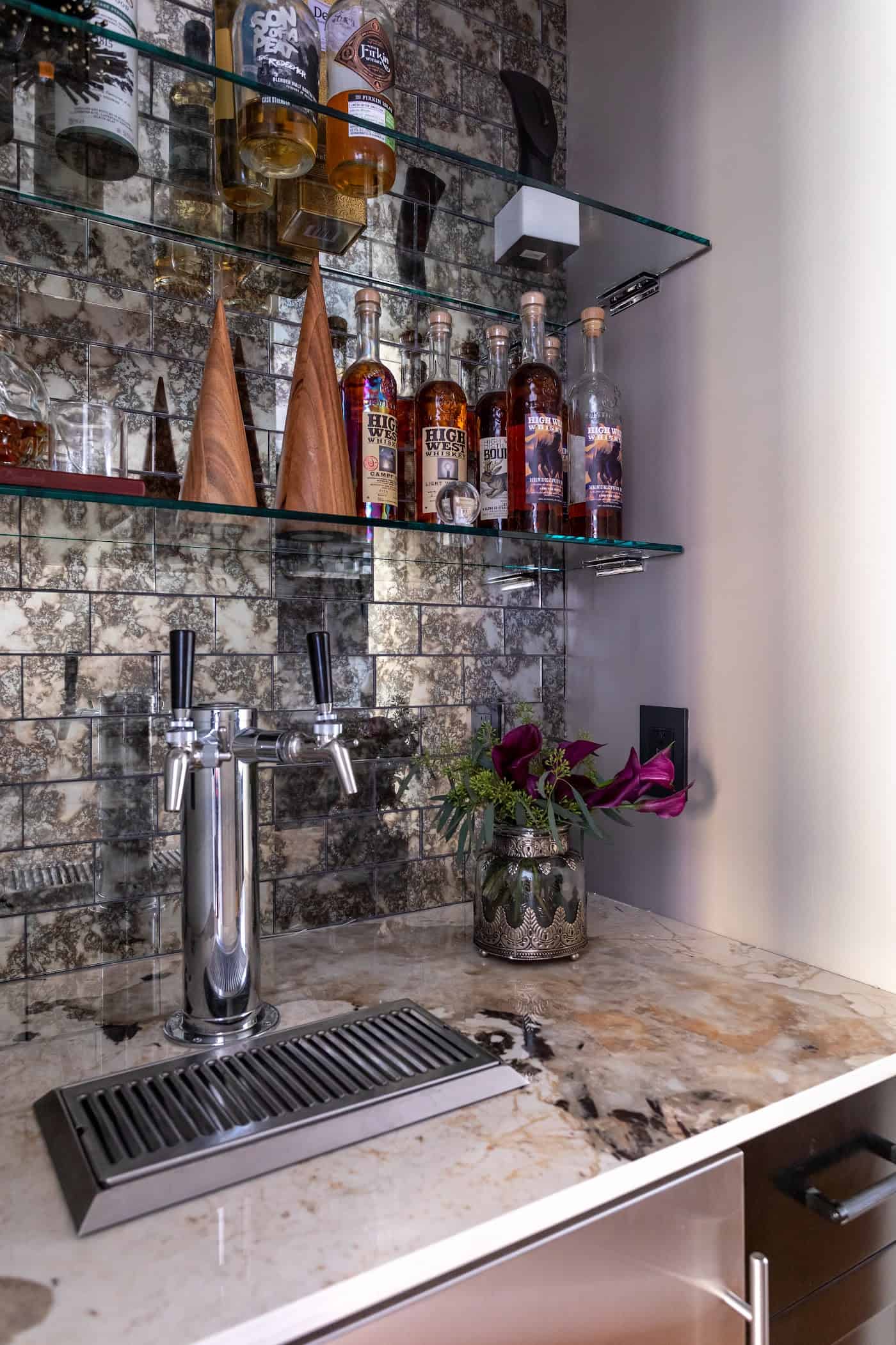 Home bar with glass shelving, beer tap and mirrored backsplash designed by The Couture Haus